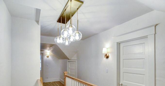 Chandelier lights hang above a staircase, with two accent lights on the white wall behind 